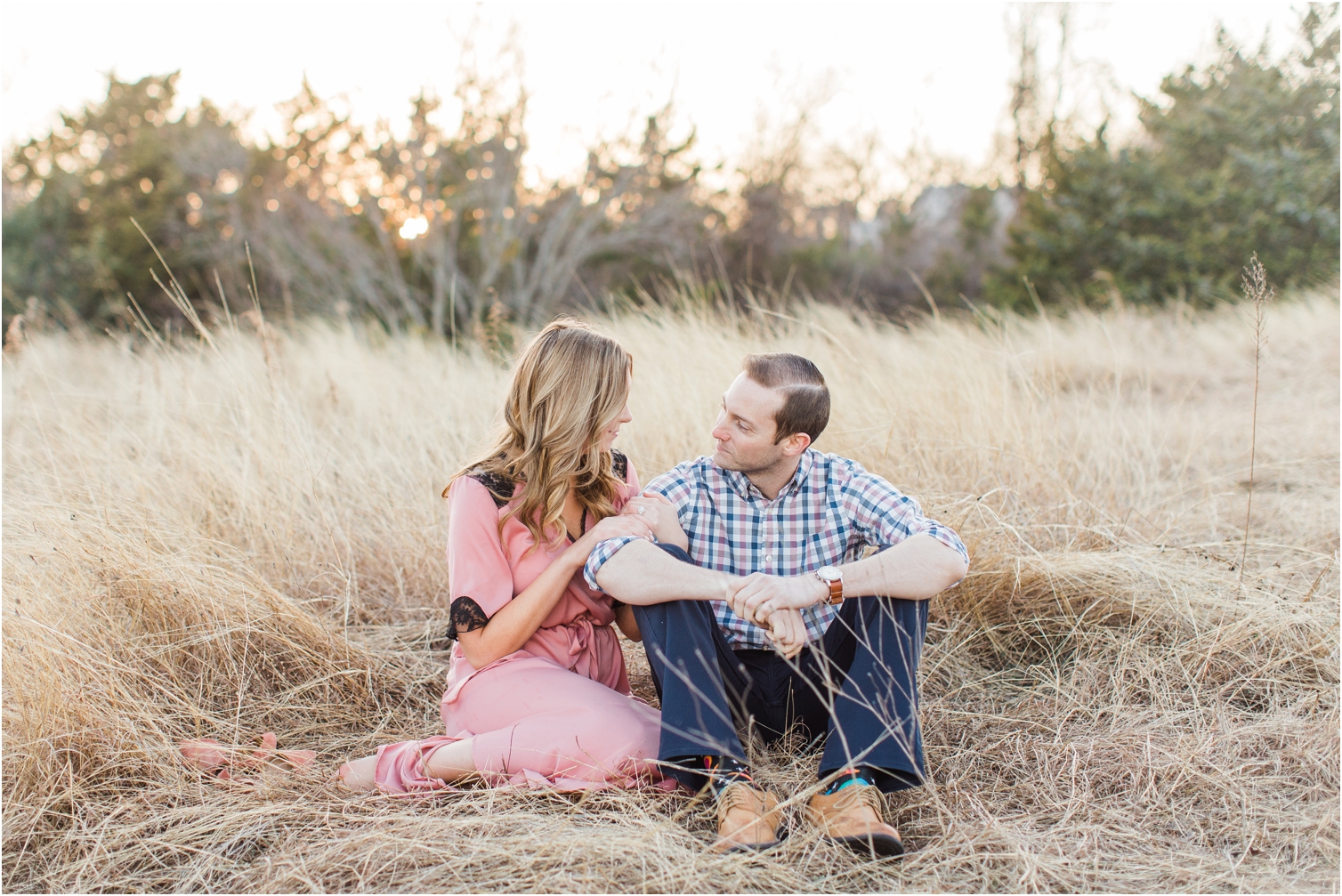 engaged couple sitting in field during golden hour